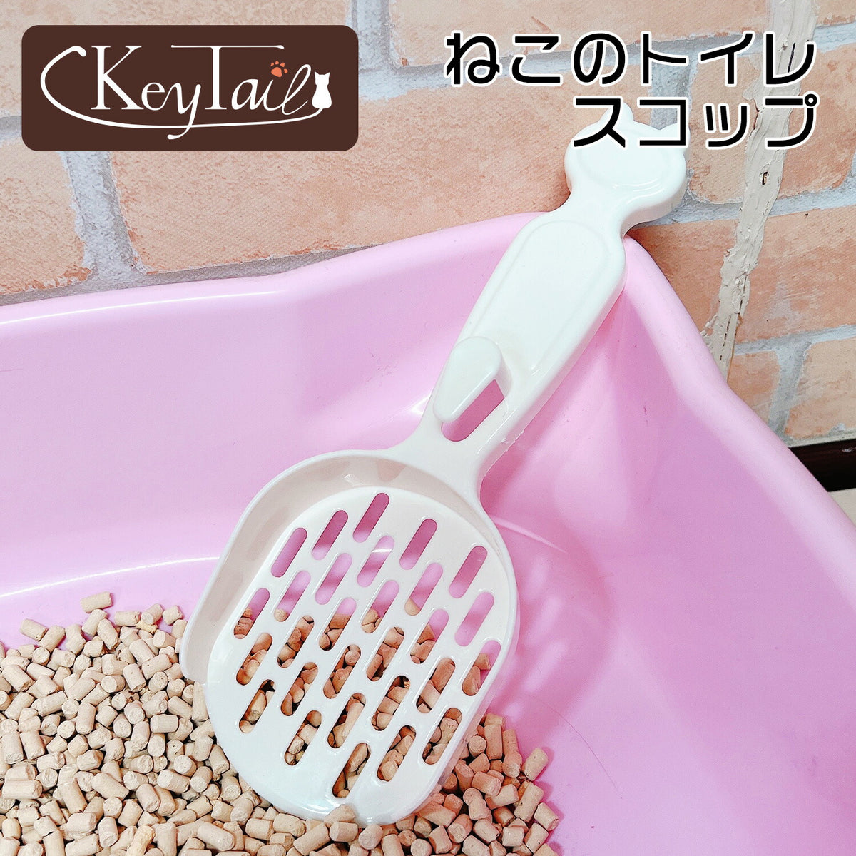 「ねこのトイレスコップ」のロゴ入り紹介カット。アイボリーの猫耳型スコップがピンクのトイレ容器に立てかけられ、目の細かい網目で小粒の猫砂をすくっている