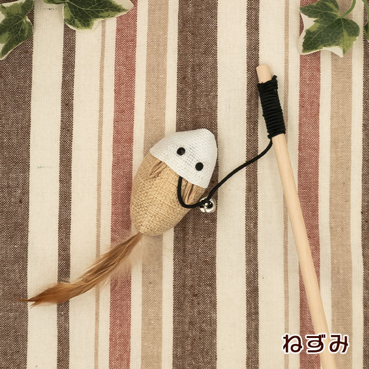 ねずみ型チャーム。白い頭部と麻布の胴体、茶色い羽根の尻尾、鈴付き。木製の柄とストライプ生地の上に配置
