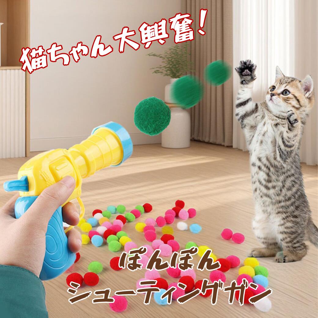 ふわふわポンポンシューティングガンで緑のポンポンボールを撃ち、後ろ足で立って前足を伸ばし追いかける子猫。手前には黄色と水色のガン本体とカラフルなボールが散らばる