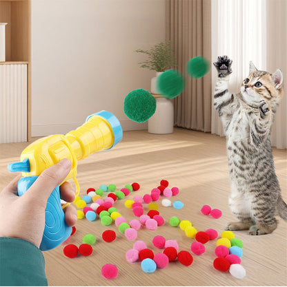 室内でガンから緑のポンポンボールが連続発射され、後ろ足で立った子猫が前足を伸ばして追いかける様子。床にはカラフルなボールが散らばる