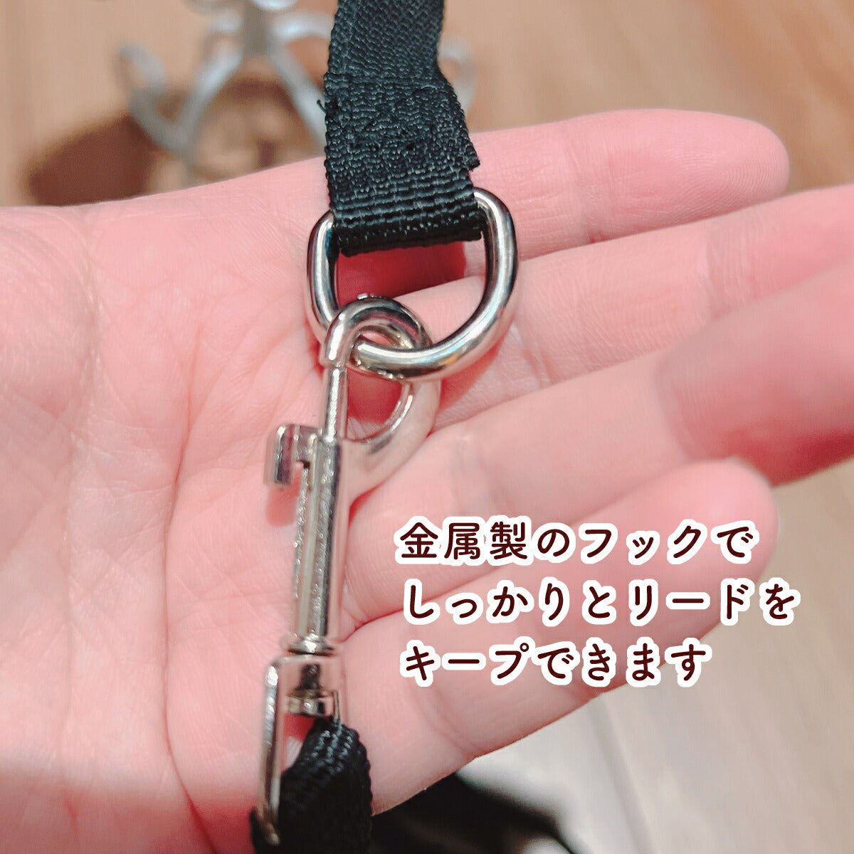 手のひらに乗せた金属製の丸カンとナスカン(フック)の接写。「金属製のフックでしっかりとリードをキープできます」のコピー