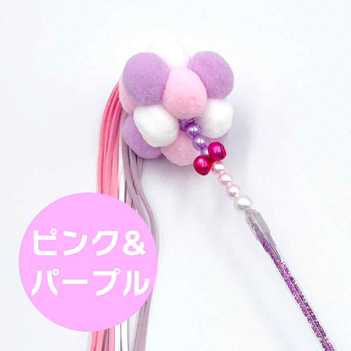 ピンク＆パープルカラーのもこもこボール部分のクローズアップ写真。紫・白・ピンクのポンポンと赤い鈴付きビーズが写る