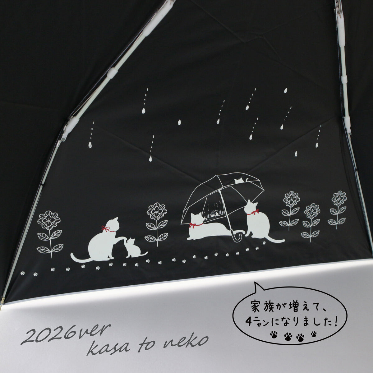 傘を開いた内側のアップ。黒地に白い猫の親子や雨傘をさす猫たちのイラストと雨粒模様。「家族が増えて、4ニャンになりました!」の吹き出しと「2026ver kasa to neko」の文字