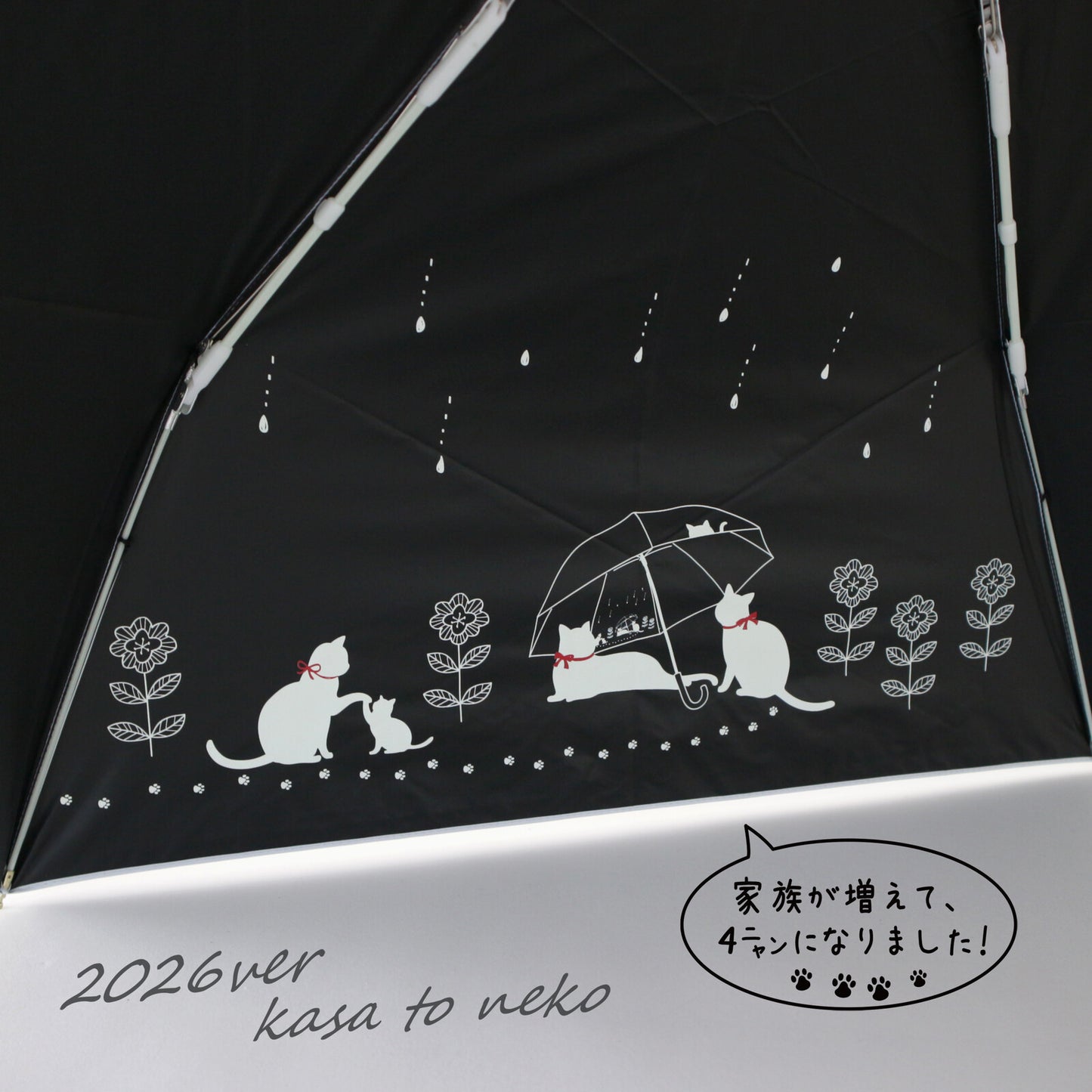 傘を開いた内側のアップ。黒地に白い猫の親子や雨傘をさす猫たちのイラストと雨粒模様。「家族が増えて、4ニャンになりました!」の吹き出しと「2026ver kasa to neko」の文字