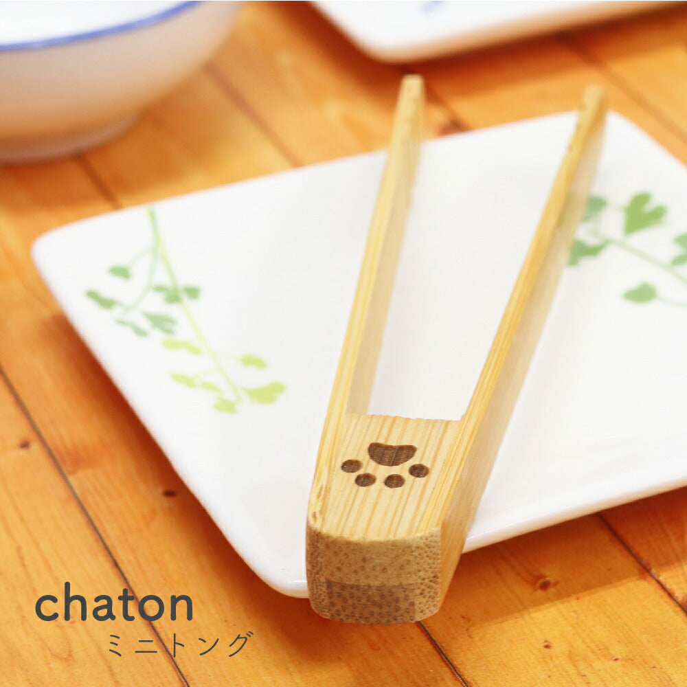 chaton ミニトングの使用例。肉球柄が彫られた竹製トングが、葉柄の白い角皿にちょこんと立てかけられている食卓カット