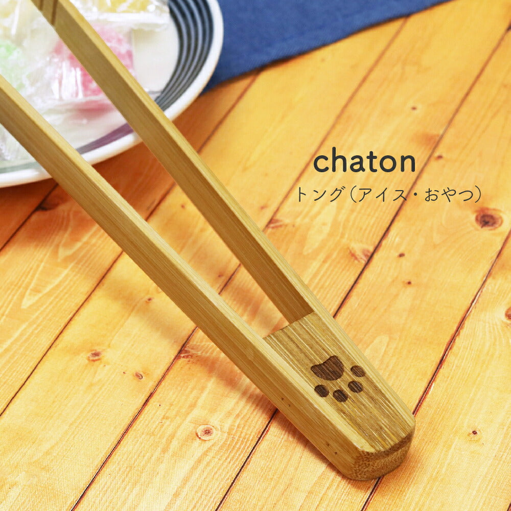 天然竹製の肉球柄トングでキャンディを挟むクローズアップ。「chaton トング(アイス・おやつ)」の商品名表記、持ち手には肉球の焼き印