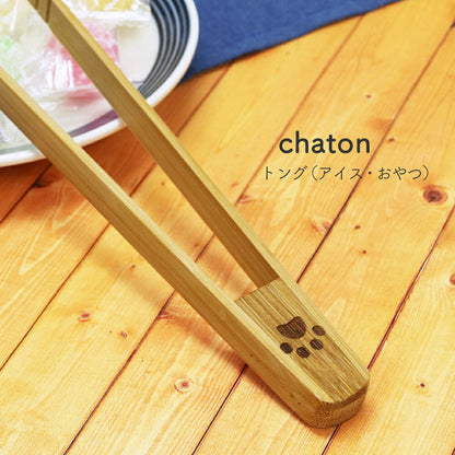 天然竹製の肉球柄トングでキャンディを挟むクローズアップ。「chaton トング(アイス・おやつ)」の商品名表記、持ち手には肉球の焼き印