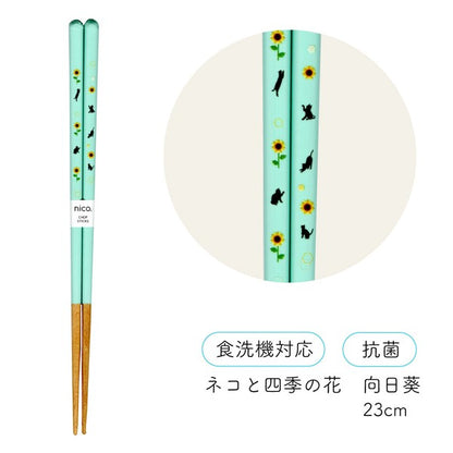 ミント色の向日葵柄。猫シルエットとひまわりの花柄が入った箸の全体と拡大図、「食洗機対応」「抗菌」表記、カラー名は向日葵・23cm