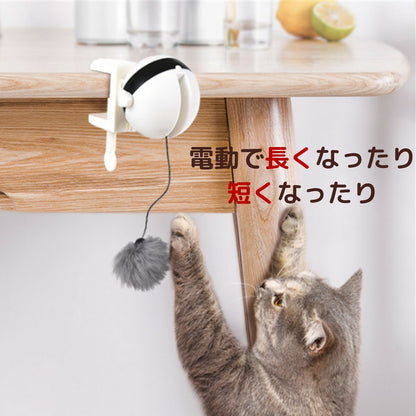 木製テーブルの天板下にクリップ固定した様子。「電動で長くなったり短くなったり」の文字と、垂れた毛玉に後ろ足で立ち上がる猫