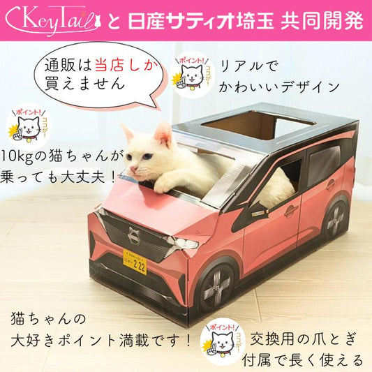 日産サティオ埼玉と共同開発、通販は当店のみで購入可能とアピール。10kgの猫が乗っても大丈夫な強度で、交換用の爪とぎボードが付属する。白猫がピンクの車型ハウスから顔を出している