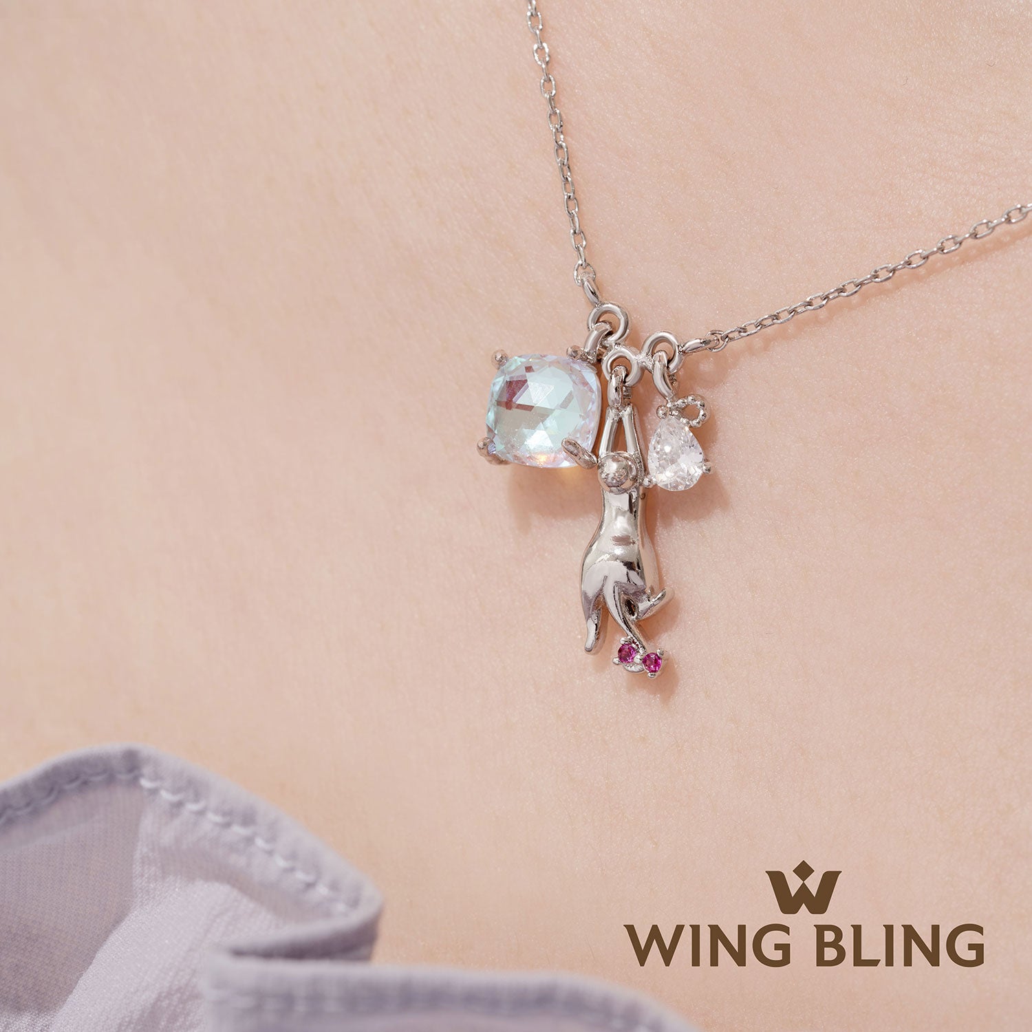 肌の上で輝くオーロラ水晶と猫シルエットチャームのアップ写真とWING BLINGロゴ。石の透明感とチャームのディテールが分かるクローズアップカット