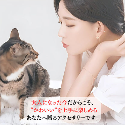 顔を寄せ合う女性と茶トラ猫。「大人になった今だからこそ、かわいいを上手に楽しめるあなたへ贈るアクセサリーです」のコピー、女性の手首にブレスレットが見える