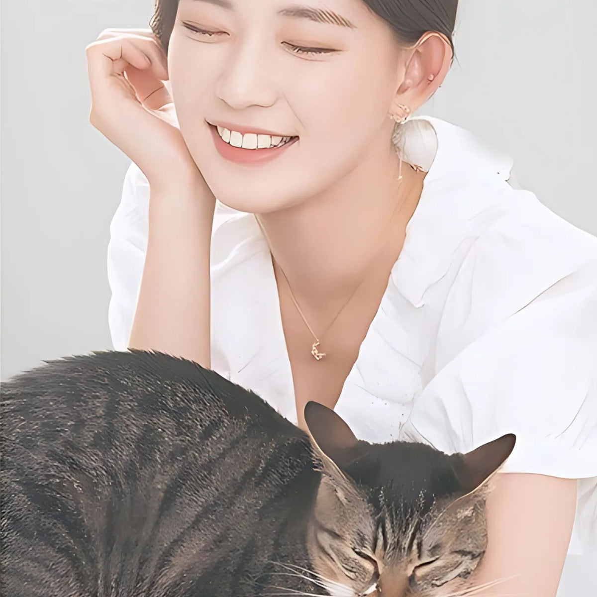 猫を抱いて微笑む女性の耳元と首元にピアスとネックレスを着けたクローズアップ