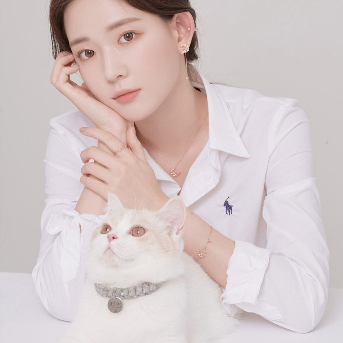 白シャツ姿で猫を抱く女性が本ピアスとネックレス、リングを着用したスタイリング写真