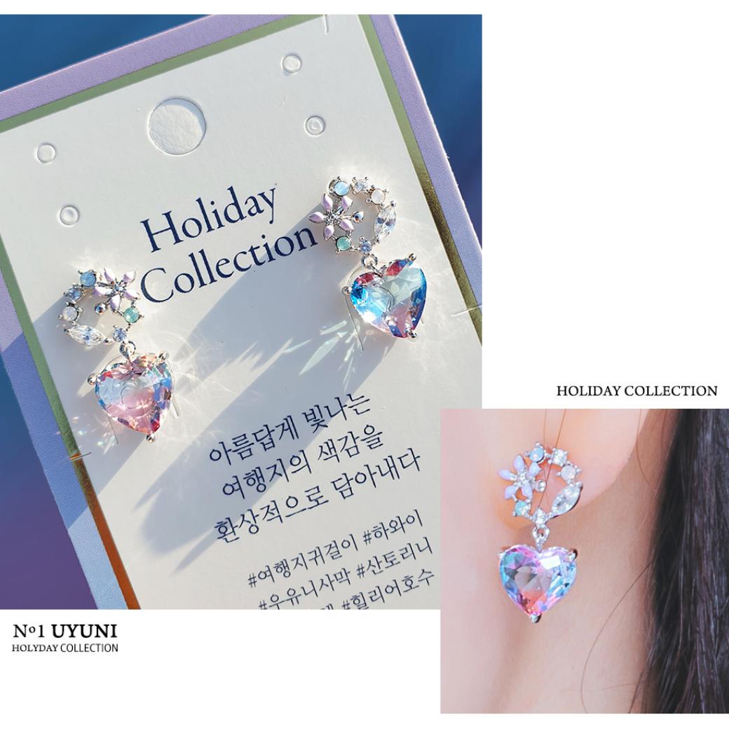 「Holiday Collection」のタグに留められたブルー×パープルのグラデーションハートピアス。ハングルで「美しく輝く旅先の色彩を幻想的に描き出す」の説明文と着用耳元カットを併記