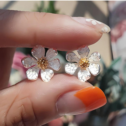 指でつまんで見せる花モチーフイヤリングの接写。立体的な花びらの質感とゴールドカラーの中心パーツが分かるアップ