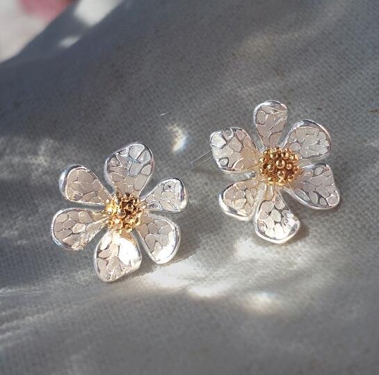 布の上に置いた花形イヤリング2個の商品写真。花びらのシルバーカラーと中心のゴールドカラーの質感が分かるアップ