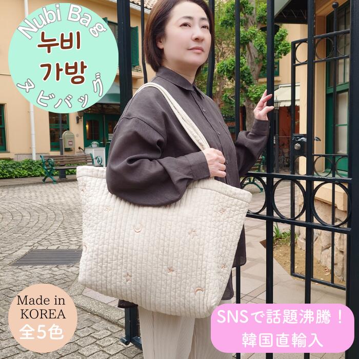 門の前でヌビバッグ マチつきLをオフホワイトの月星刺繍柄で肩掛けする女性。韓国製・全5色、SNSで話題の韓国直輸入キルティングバッグ