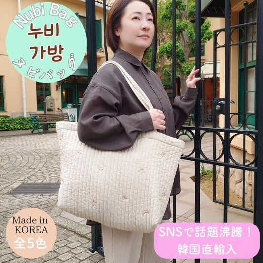 門の前でヌビバッグ マチつきLをオフホワイトの月星刺繍柄で肩掛けする女性。韓国製・全5色、SNSで話題の韓国直輸入キルティングバッグ